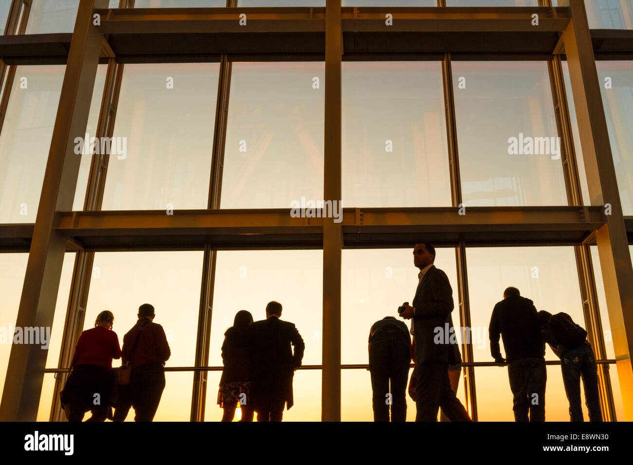 Un gruppo di persone in silhouette contro il cielo della sera guardando fuori da una finestra al di Shard, London, England, Regno Unito Foto Stock