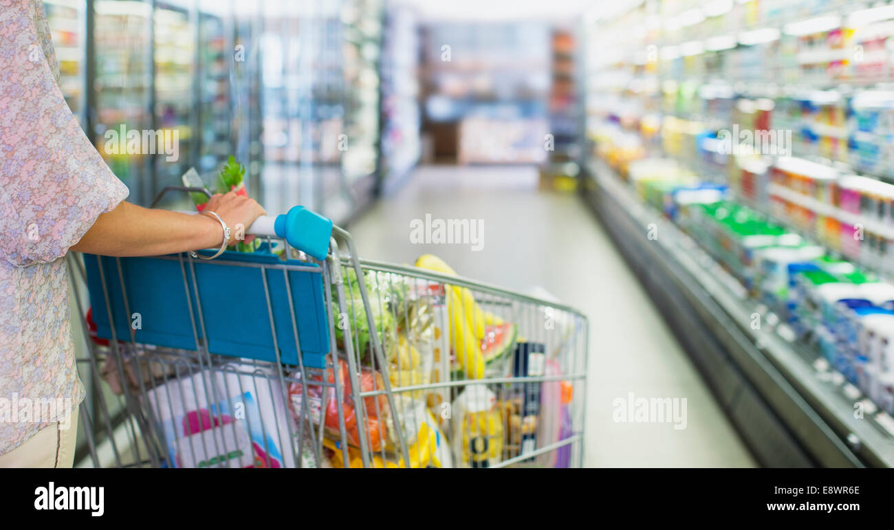 Donna piena di spinta carrello acquisti nel negozio di alimentari Foto Stock
