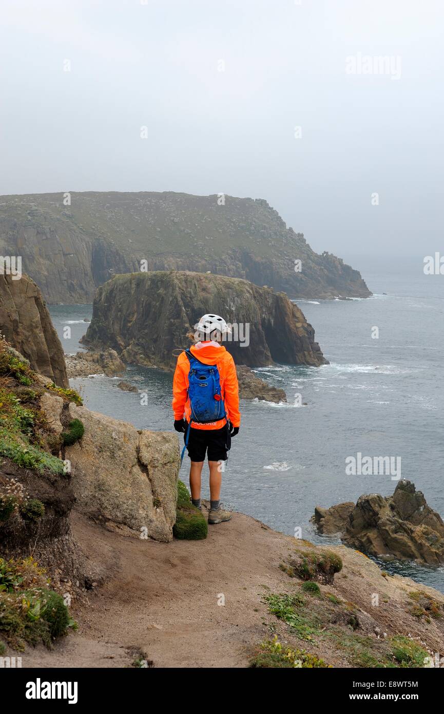 Una femmina solitario escursionista guardando oltre il ciglio della scogliera a Lands End Cornwall Regno Unito Foto Stock