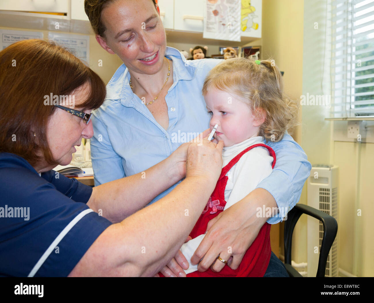 Bambino di 2 anni con la mamma / madre, riceve la dose di Fluenz vaccino antinfluenzale spray nasale immunizzazione dalla pratica di NHS nurse REGNO UNITO Foto Stock