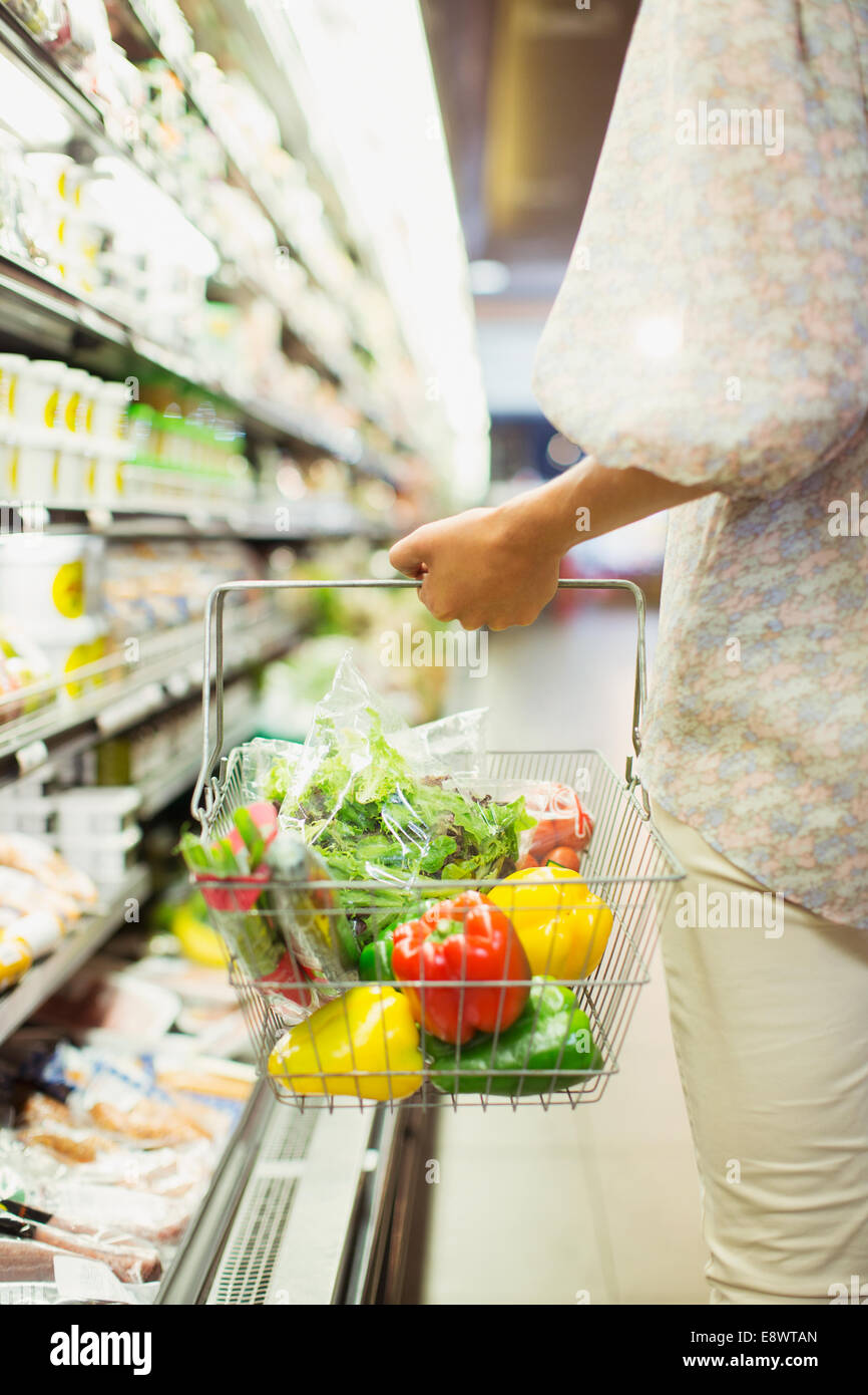 La donna che porta la piena Shopping basket in negozio di alimentari Foto Stock