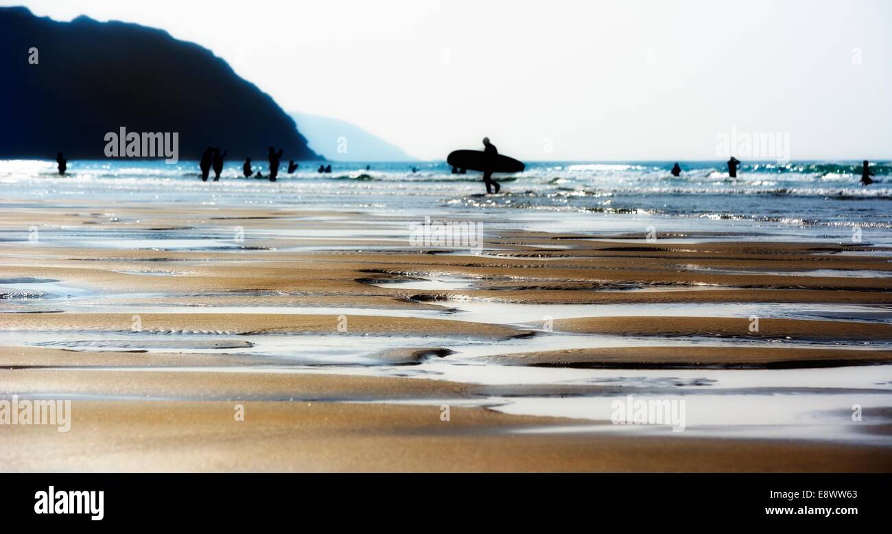 Un uomo che porta una tavola da surf sulla spiaggia a Perranporth Cornwall Inghilterra Regno Unito Foto Stock