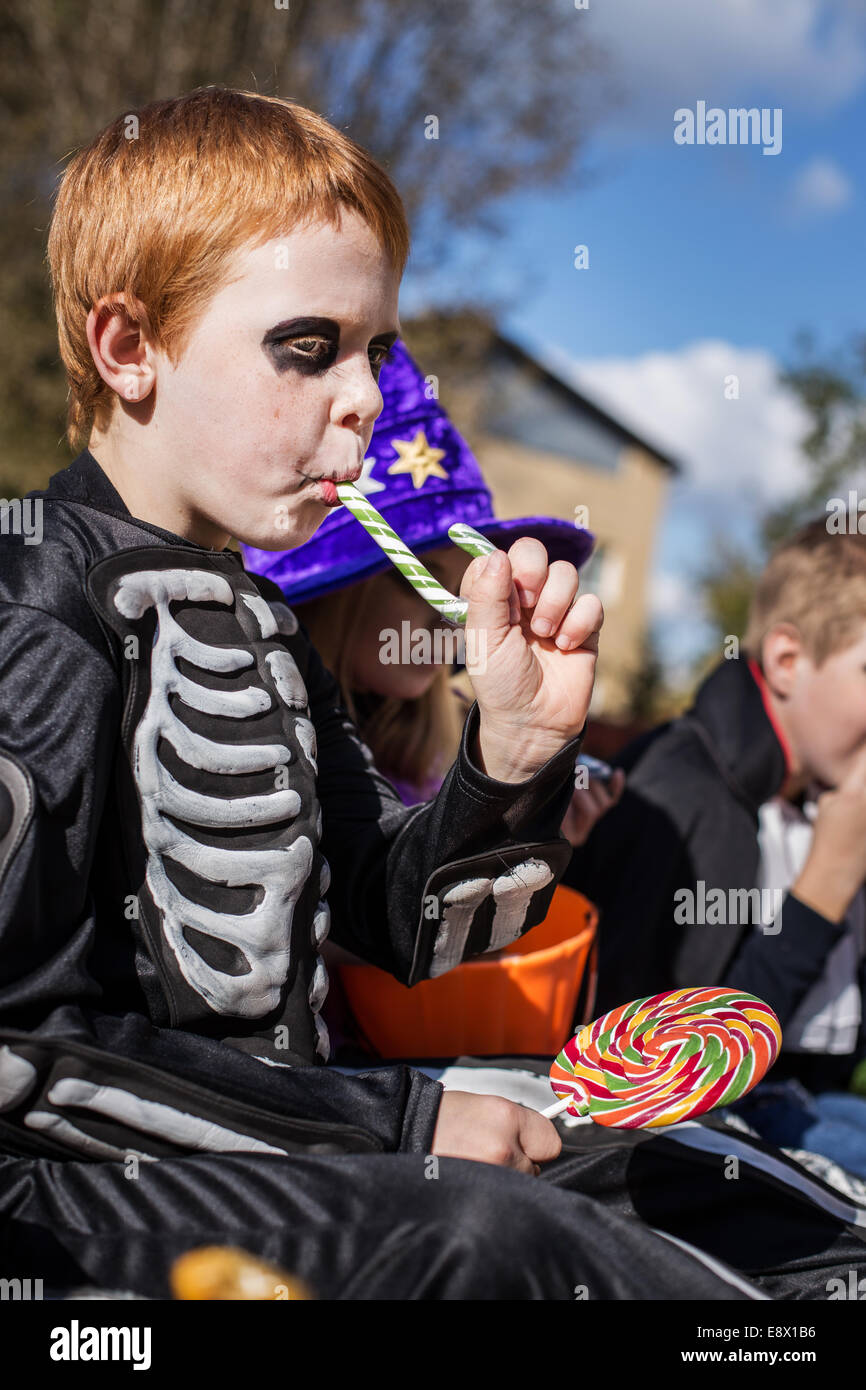 Dai capelli rossi bambino con costume scheletro mangiando caramelle colorate. Halloween Foto Stock