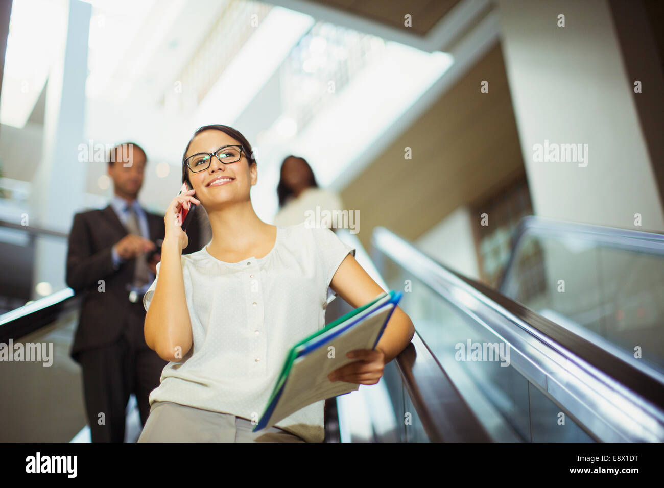 Imprenditrice parlando al cellulare mentre scendendo escalator Foto Stock