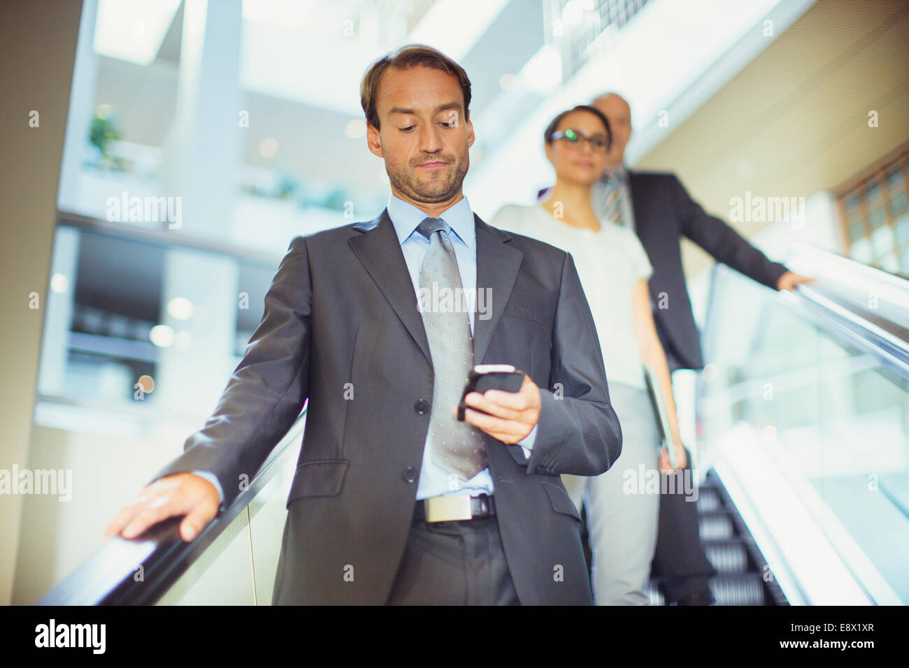 Imprenditore tramite cellulare di escalator in edificio per uffici Foto Stock