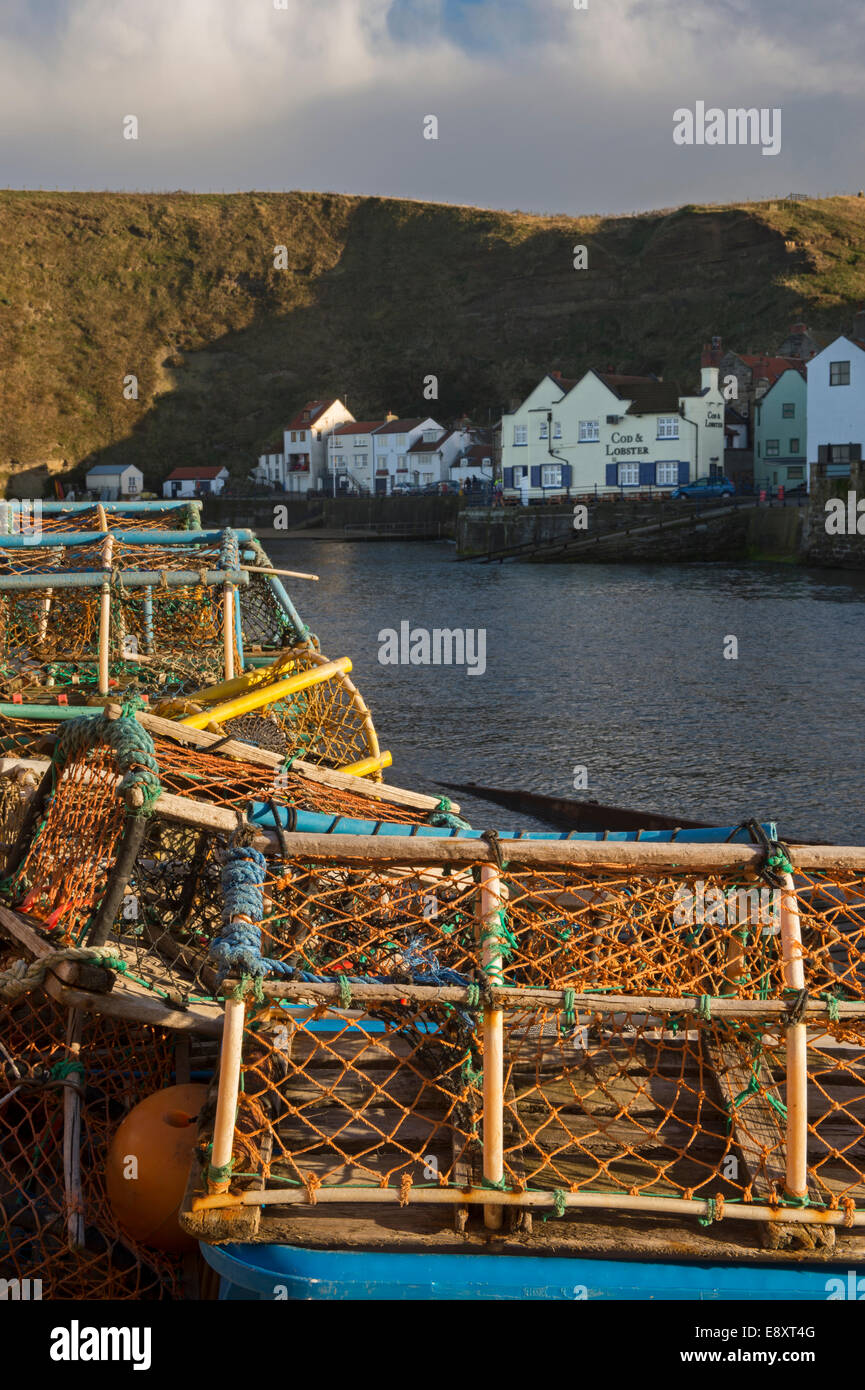 Soleggiato aragosta bicchieri impilati in una pila, con Harbour, edifici e alte scogliere al di là - mare villaggio di pescatori di Staithes, North Yorkshire, Inghilterra. Foto Stock