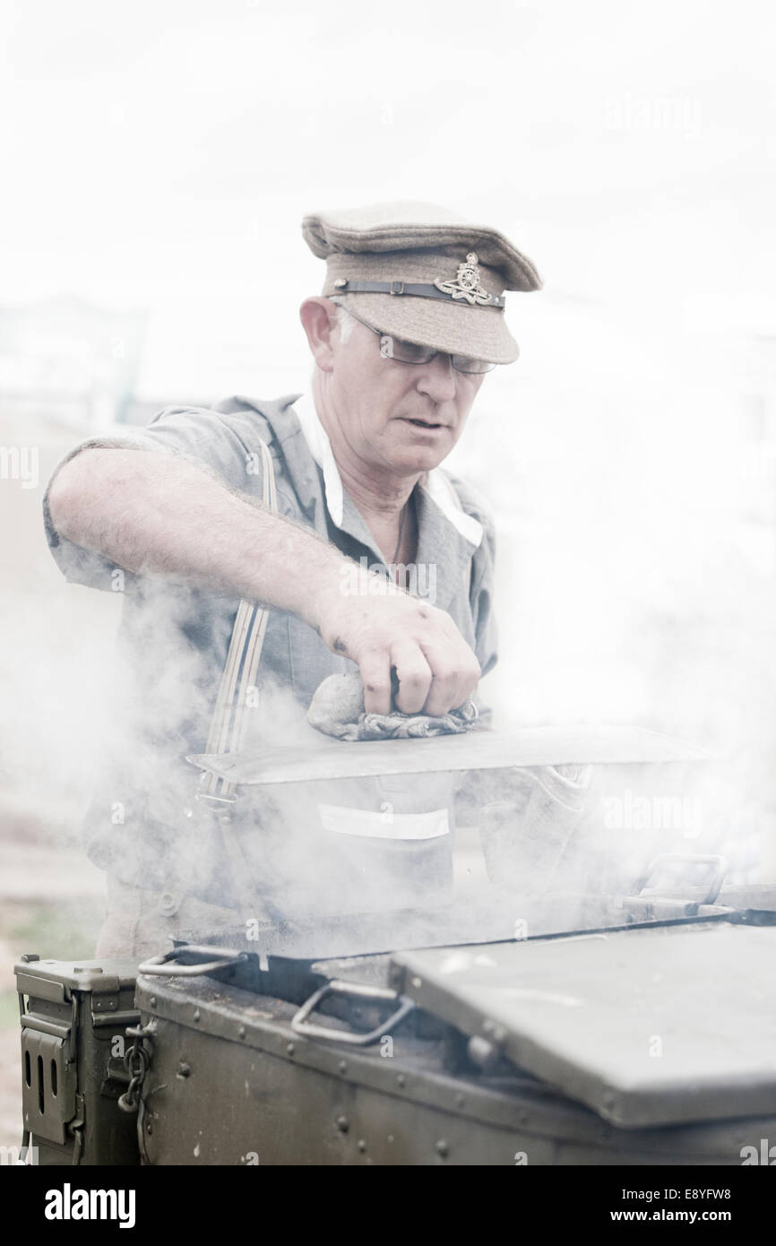 Un uomo in WW1 britannico soldati dell esercito uniforme di preparare il cibo con un cavallo disegnato da cucina di campo, il vapore caldo è in aumento dal fornello coperchio. Foto Stock
