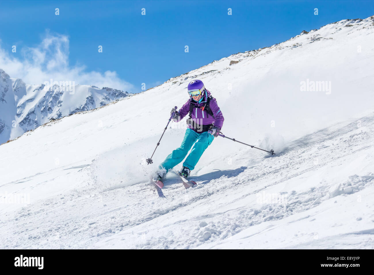 Femmina di Sciatore fuori pista sullo sfondo delle alte montagne. A sua volta solleva la polvere di neve. Foto Stock