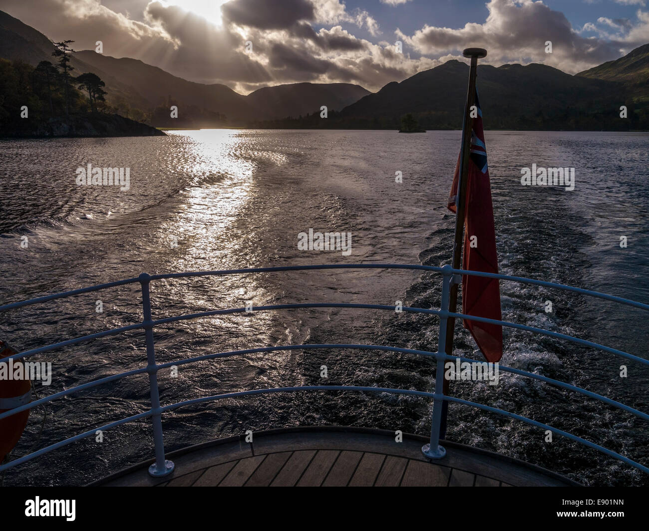 La luce del sole sulle acque del lago Ullswater e con montagne in lontananza si vede dalla poppa di 'Raven' sistema di cottura a vapore, Cumbria, England, Regno Unito Foto Stock