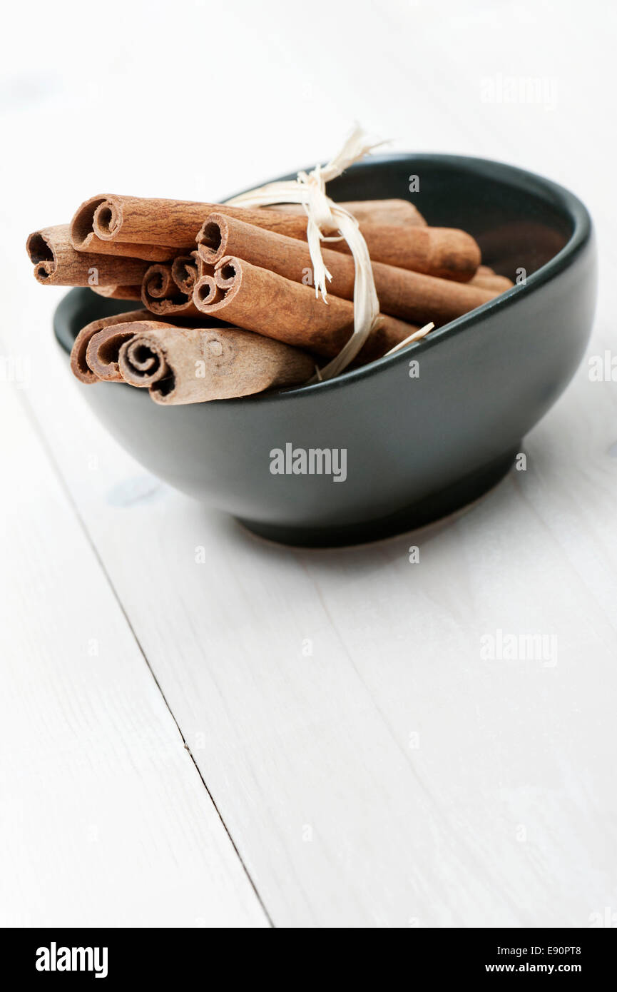 Tazza nera con bastoncini di cannella sul tavolo di legno, vista diversa Foto Stock
