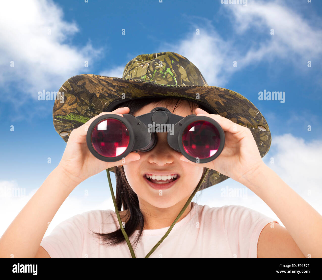 Asian sorridente bambina guardando attraverso il binocolo con blu e Sfondo nuvola Foto Stock