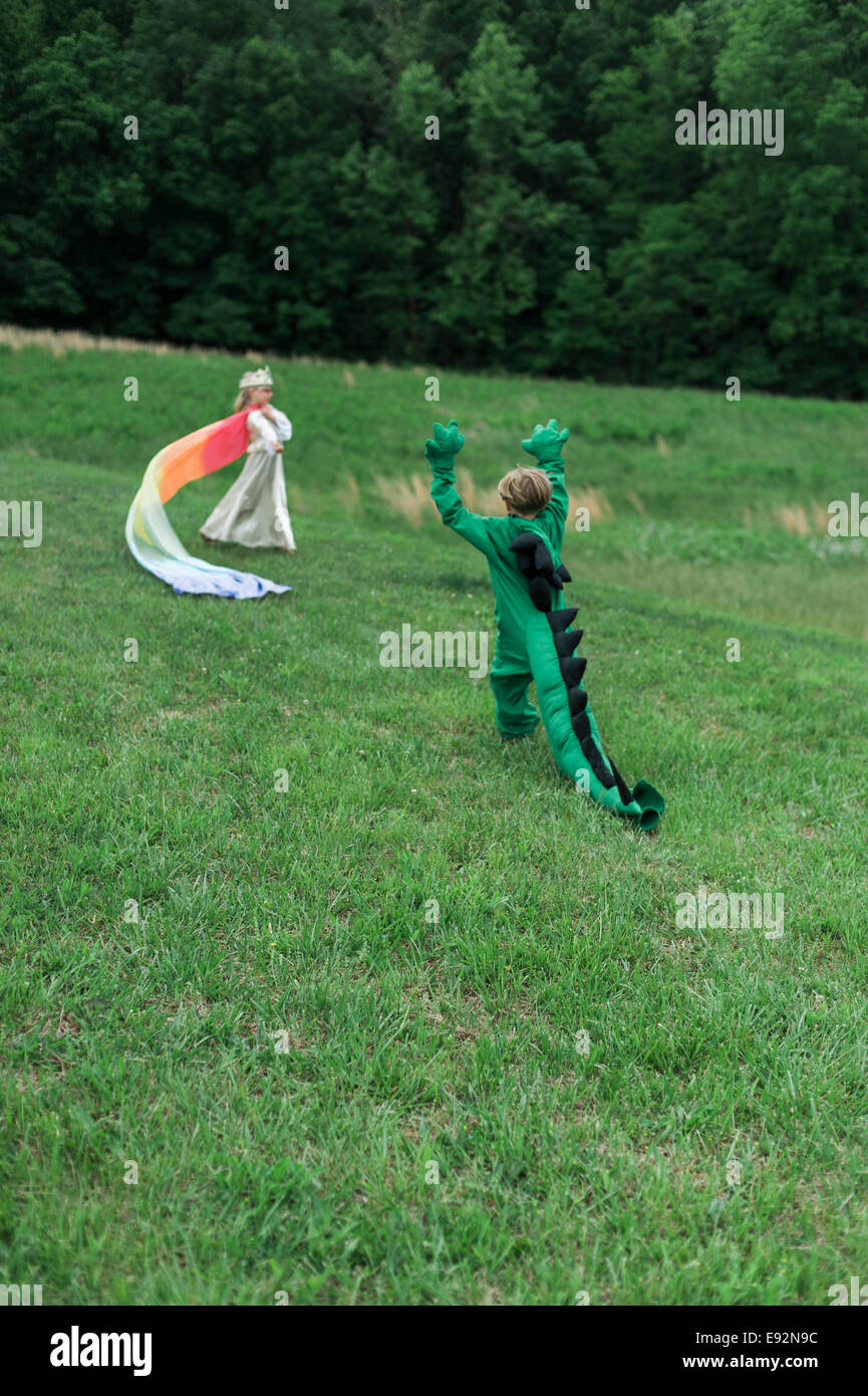 Giovane ragazzo in costume di drago giocando con la fanciulla in Costume principessa in campo erboso Foto Stock