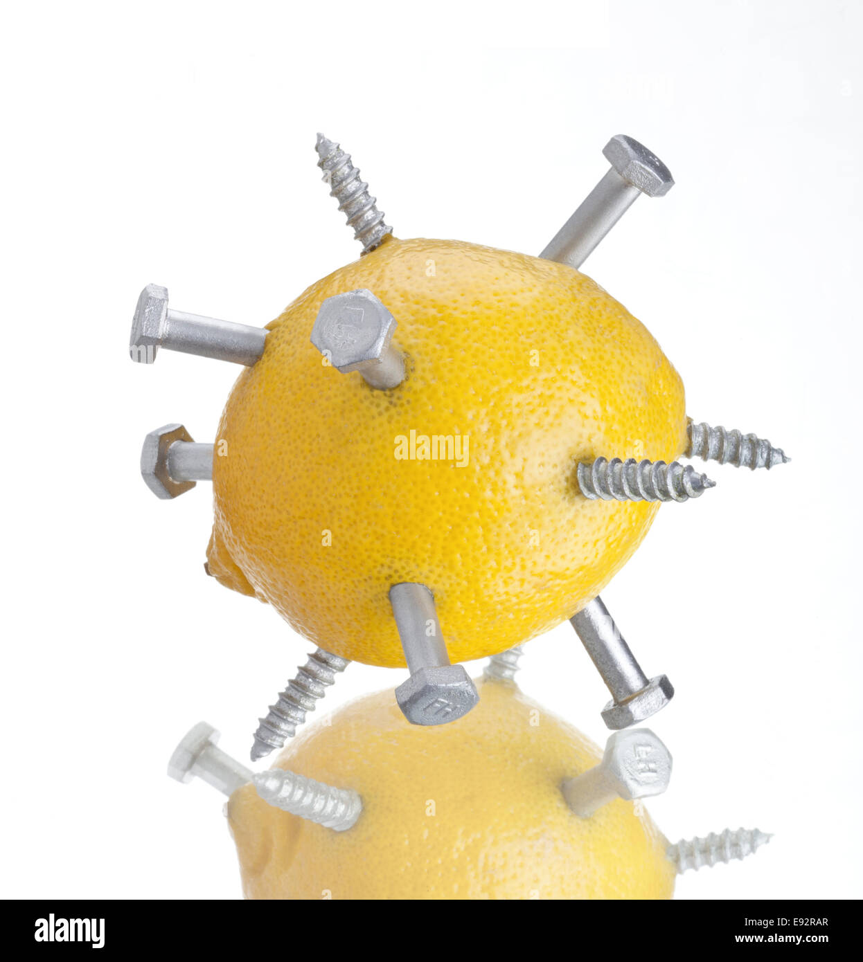 Limone giallo lucido con bulloni metallici piercing la buccia su una superficie riflettente Foto Stock
