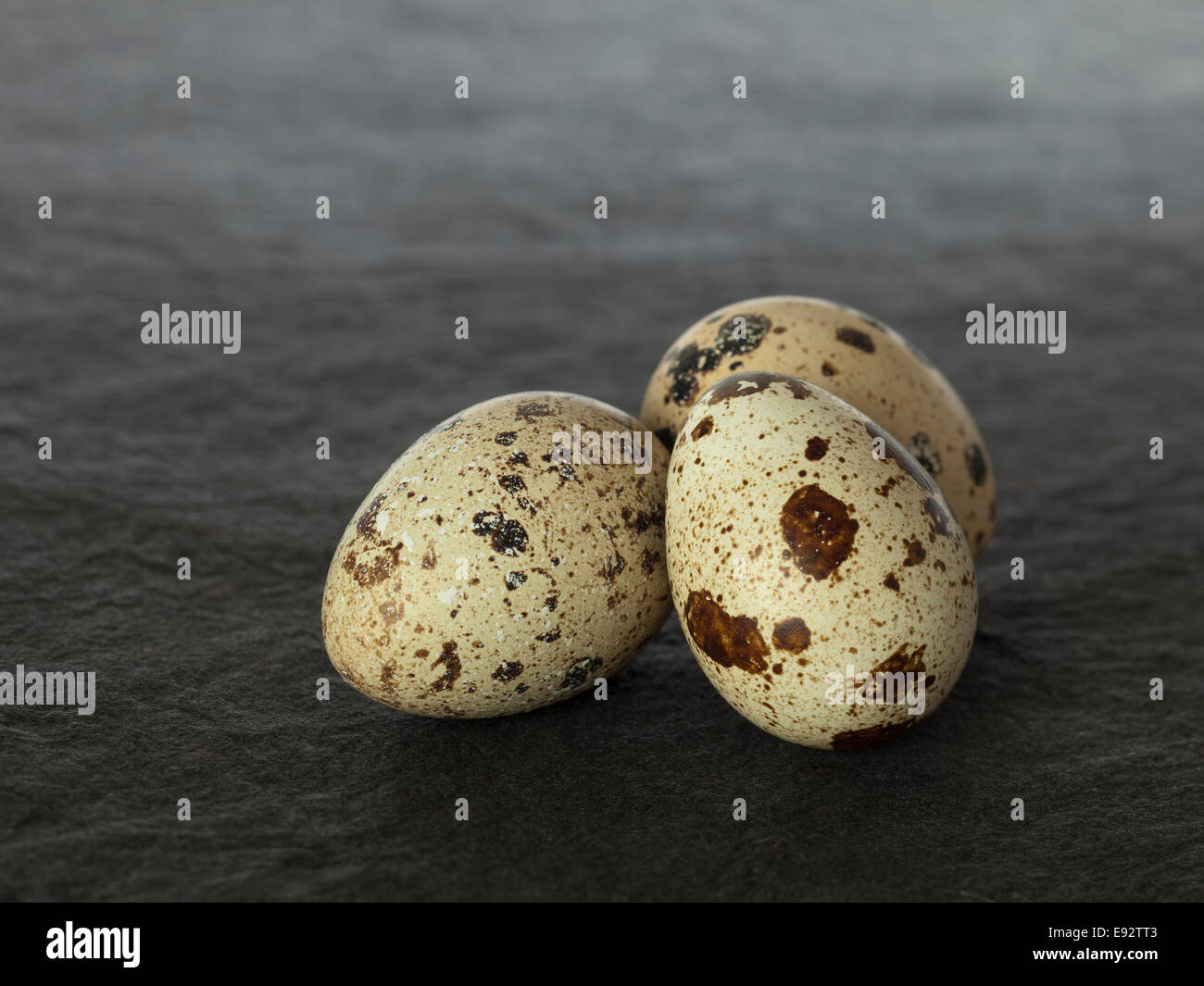 Tre spotted uova di quaglia al buio su un superficie testurizzata Foto Stock