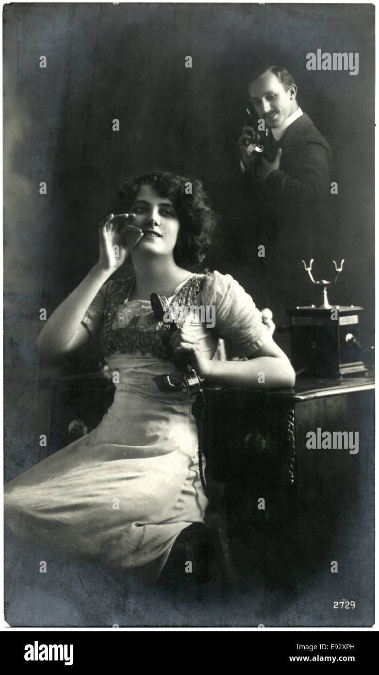 Donna che mantiene il ricevitore del telefono con l'uomo parlando al telefono in background, cartolina francese Foto Stock