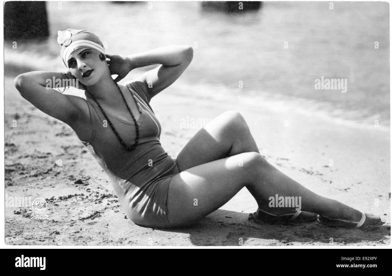 Donna monopezzo in costume da bagno e cappuccio reclinata sulla spiaggia con le mani dietro la testa, cartolina francese Foto Stock