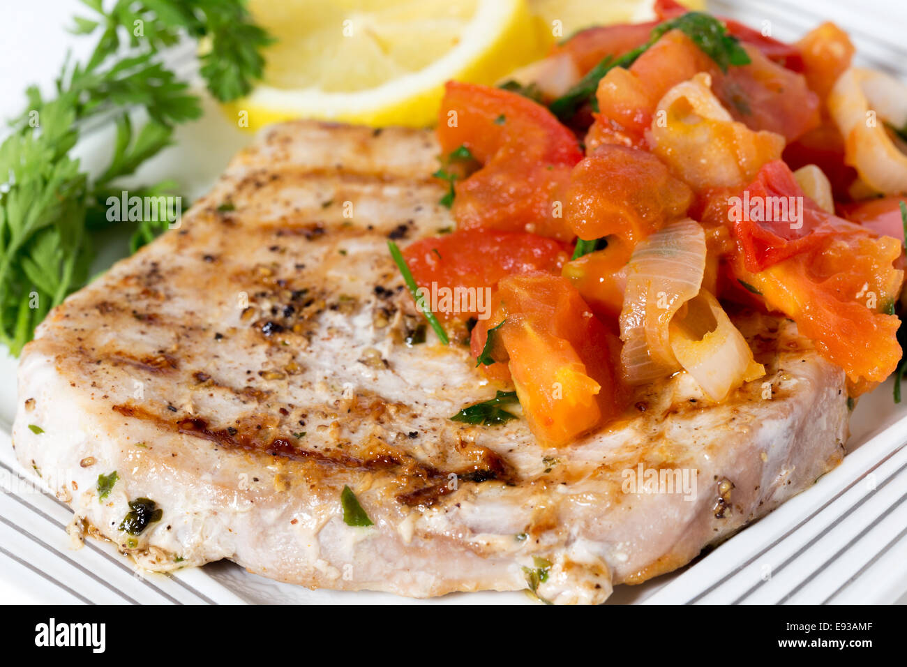 Marlin bistecca cotta su una piastra con salsa di pomodoro, limone e prezzemolo visto di lato Foto Stock