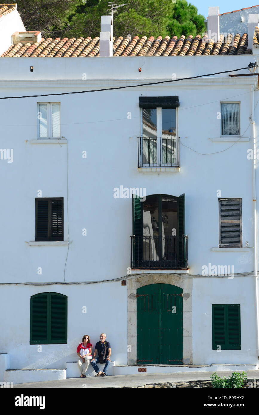 Un giovane seduto su una panchina di fronte di una tipica casa catalana durante il tentativo di rinfrescarvi nella città di Cadaques, Catalunya. Foto Stock