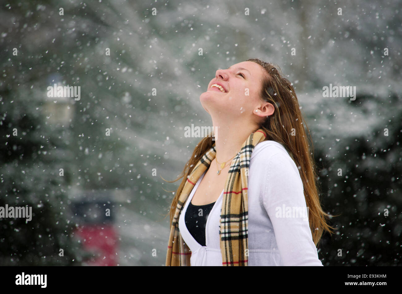 Let it Snow: una giovane donna alza le braccia nella vittoria di una bella doccia di neve. Foto Stock