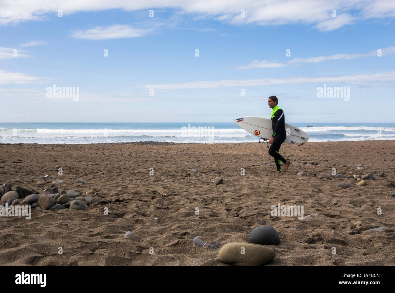 Giovane maschio camminare su una spiaggia di sabbia, portante una tavola da surf. Foto Stock