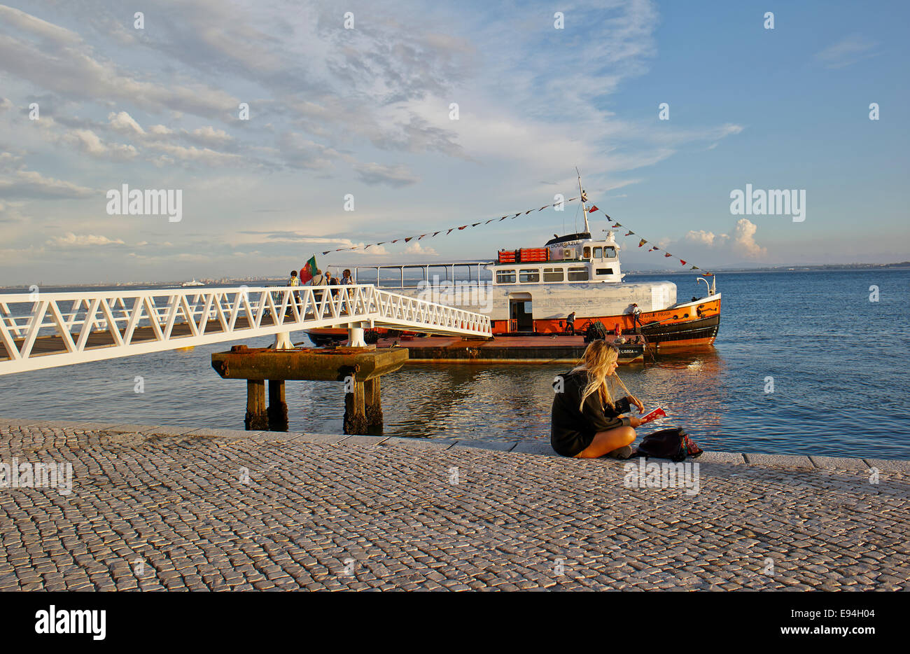 Giovane donna in attesa sulla spiaggia la sera, nave traghetto sul Tago, Tejo, fiume, Oceano Atlantico a Baixa Pombalina, Lisbona, Portogallo Foto Stock