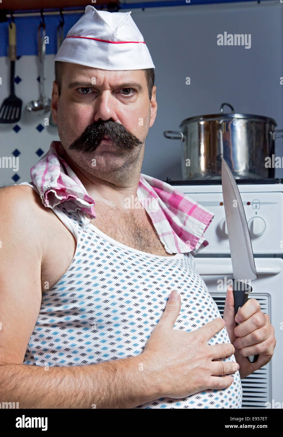Cuocere in maglietta in piedi in cucina accanto alla stufa Foto Stock