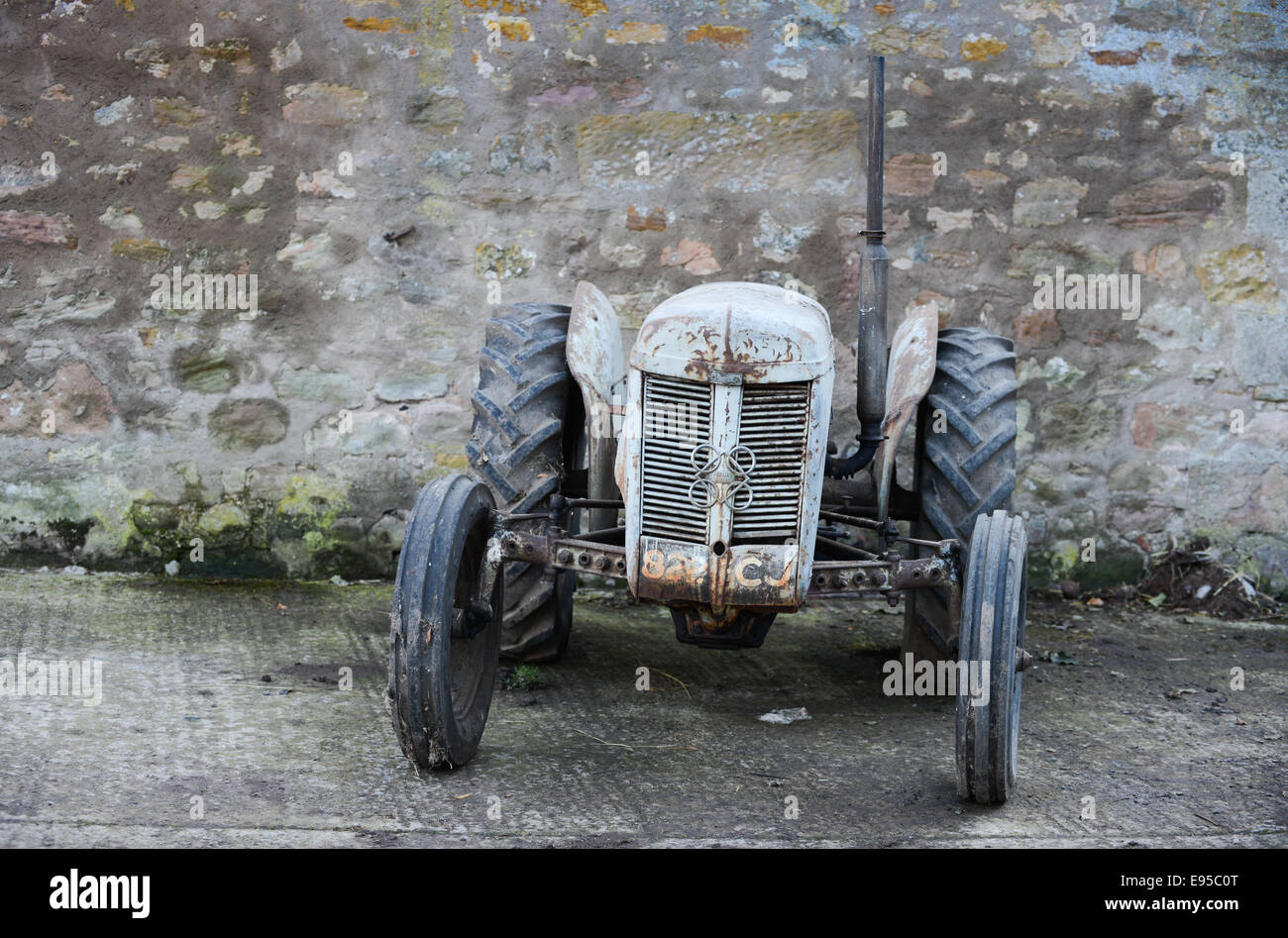 Grigio vecchio trattore contro un muro di pietra Foto Stock