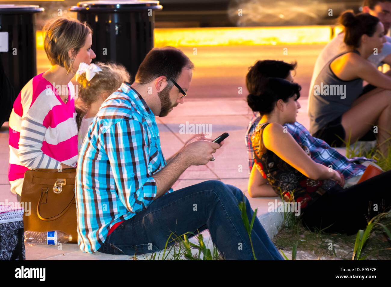 La gente seduta su un marciapiede guardando un evento con la famiglia Foto Stock