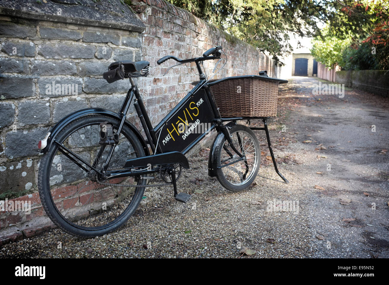 Vintage degli anni trenta bakers (Tradesman's) consegna bicicletta con cesto di vimini e la vecchia insegna la scrittura Hovis ha pannello pubblicitario. Foto Stock