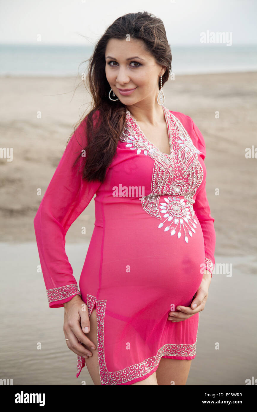 Donna incinta in bikini bianco in posa sulla spiaggia Foto Stock