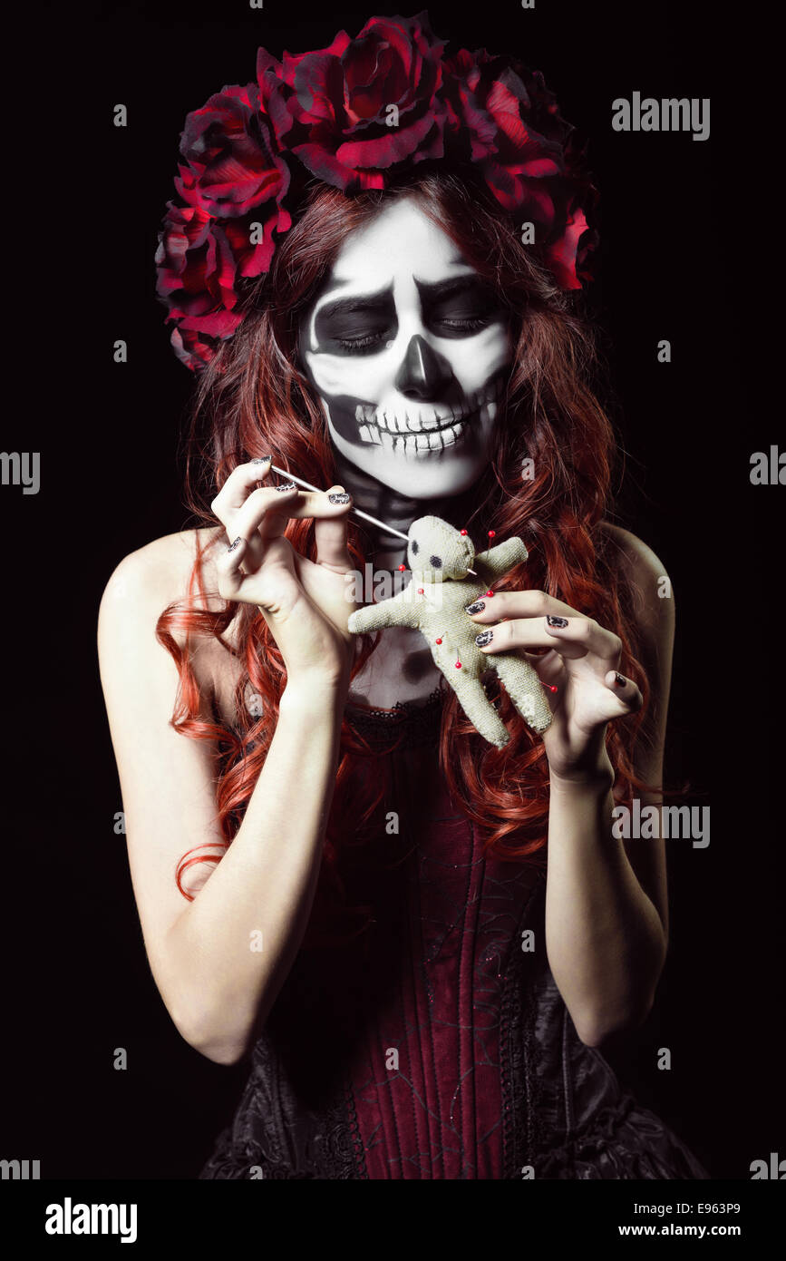 Giovane donna con il trucco calavera (zucchero cranio) perforare una bambola voodoo Foto Stock