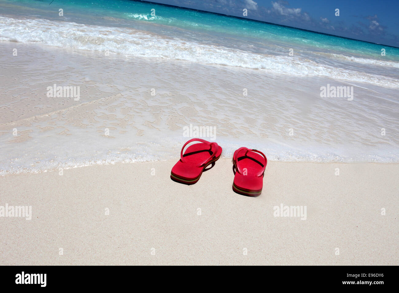 Red flip flop sulla spiaggia contro acqua chiara Foto Stock