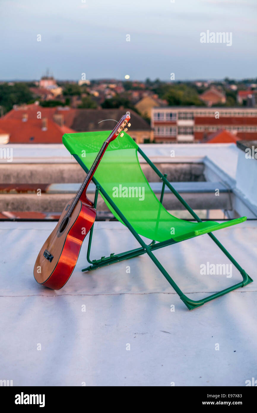 Chitarra appoggiata contro il lettino sulla terrazza sul tetto Foto Stock