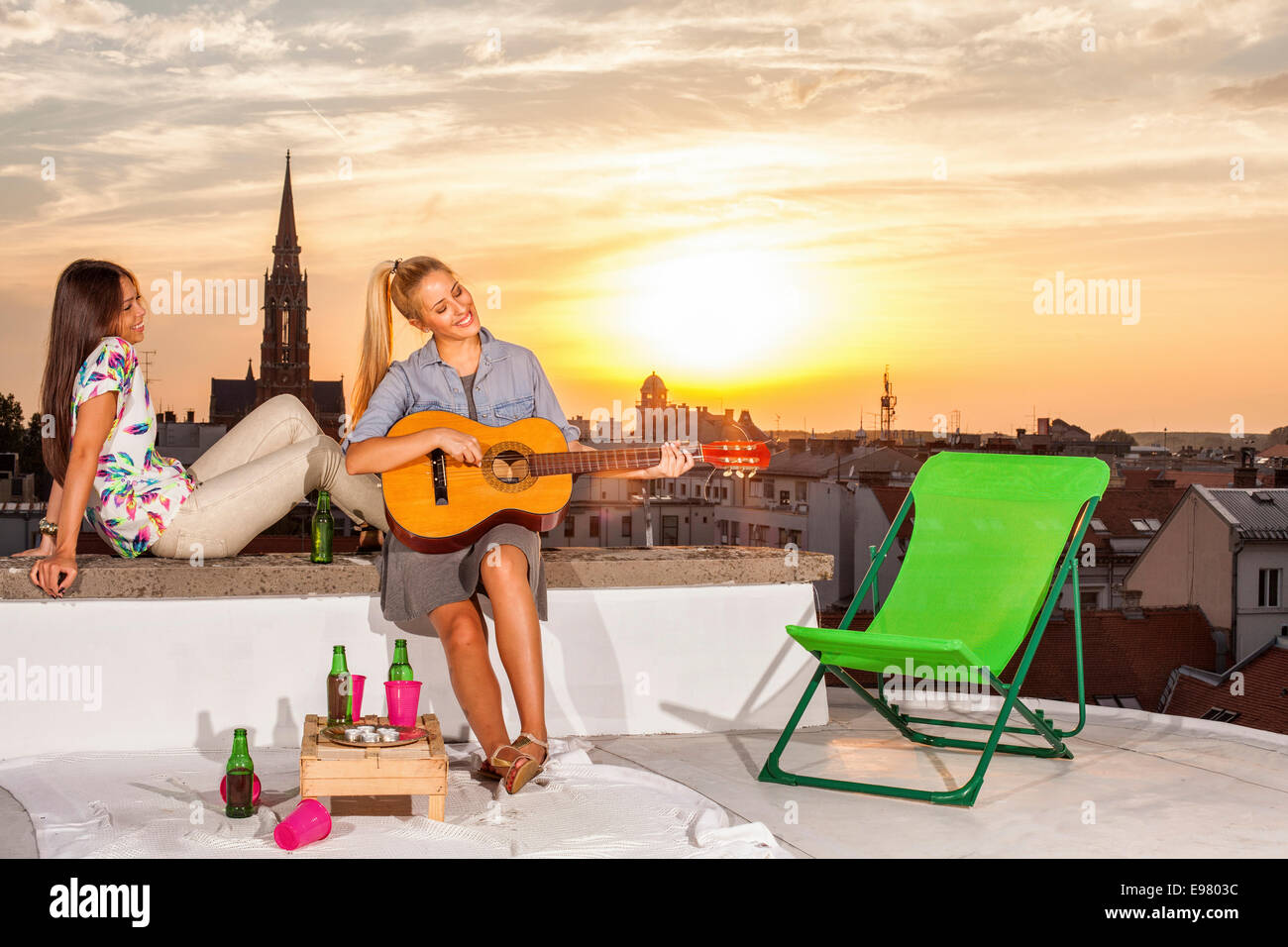 Giovane donna con la fidanzata a parte sul tetto a suonare la chitarra Foto Stock