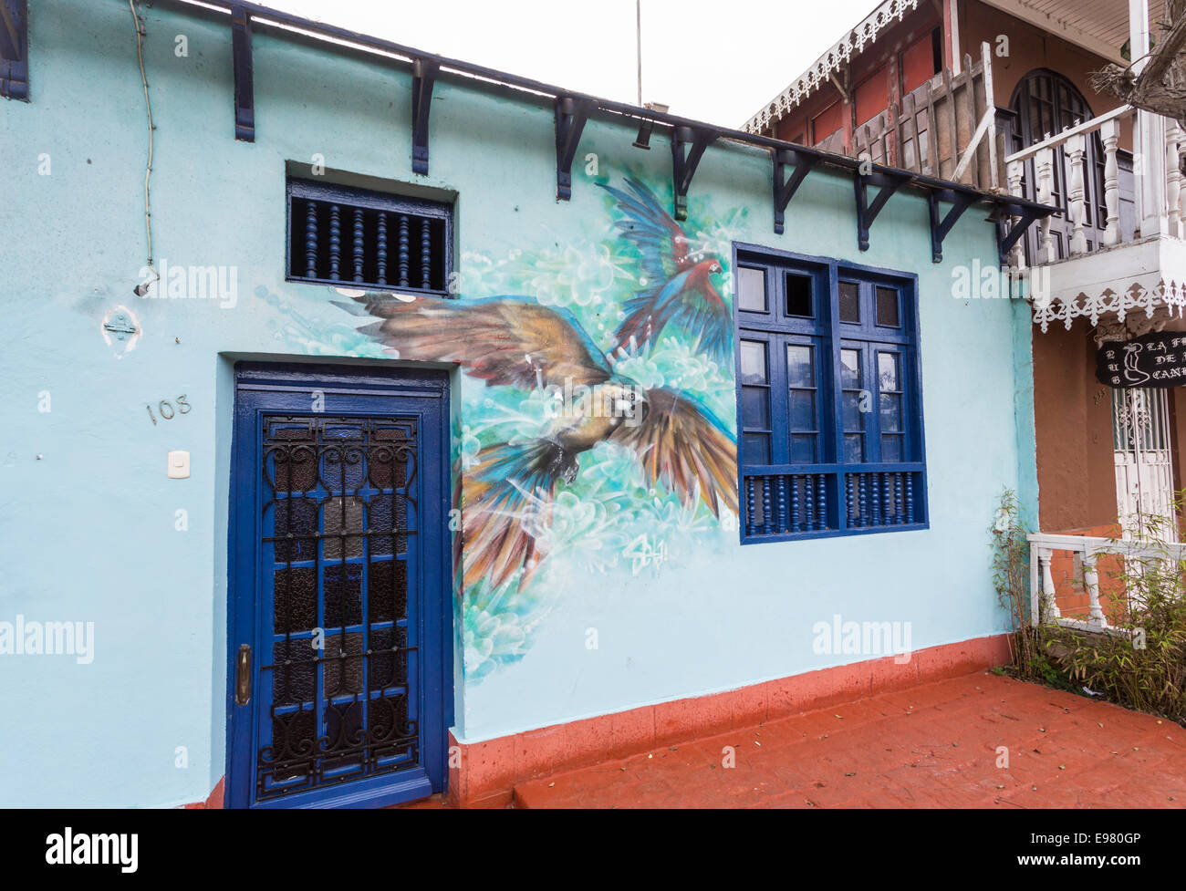 Pareti dipinte di blu colorato e ingresso ad un piccolo ristorante locale a Barranco, Lima, Peru con un dipinto murale di pappagalli in volo Foto Stock