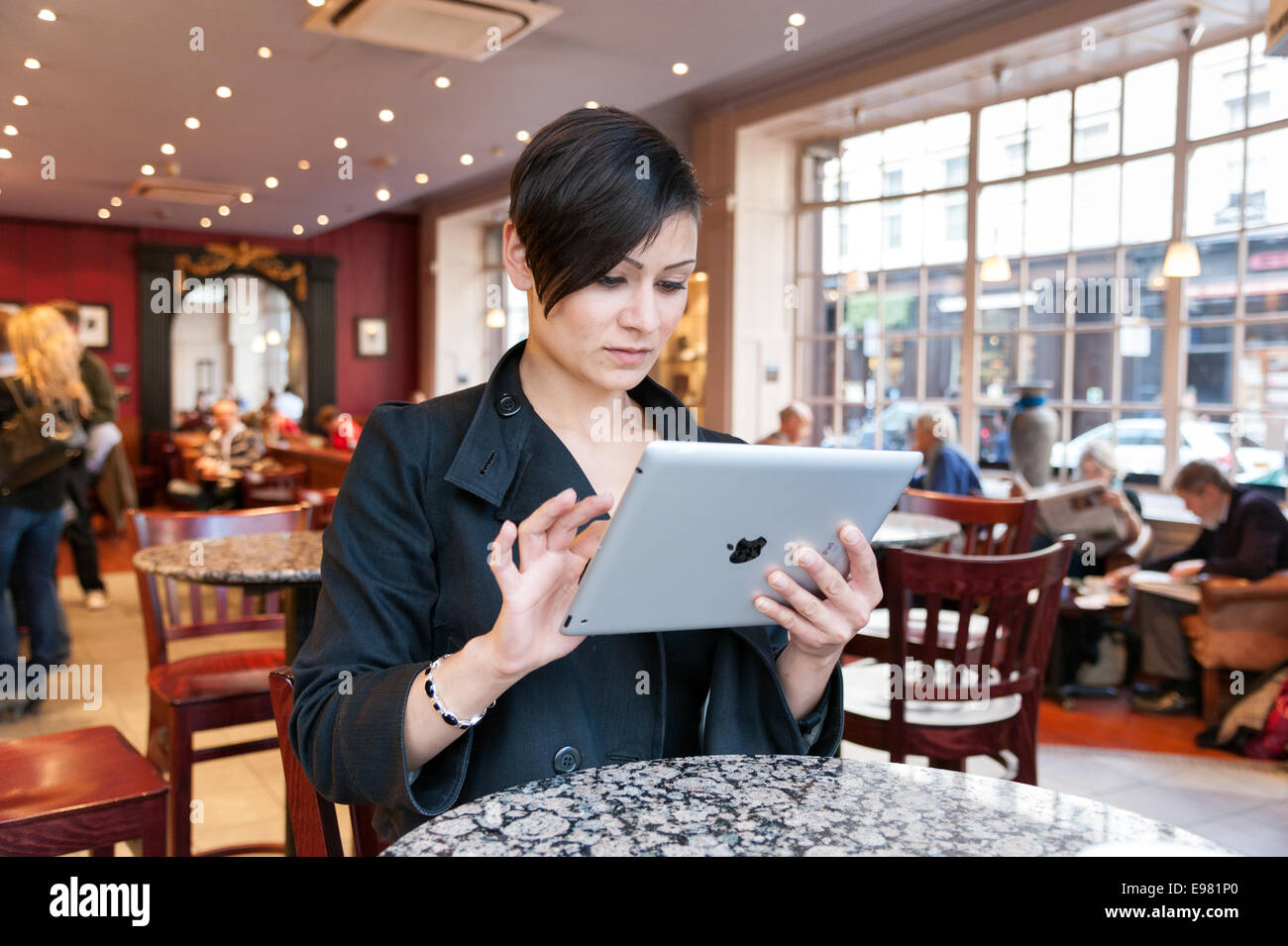 Giovane donna navigando in Internet su un iPad di Apple Computer tablet utilizzando coffee shop gratuito wi fi, London, England, Regno Unito Foto Stock