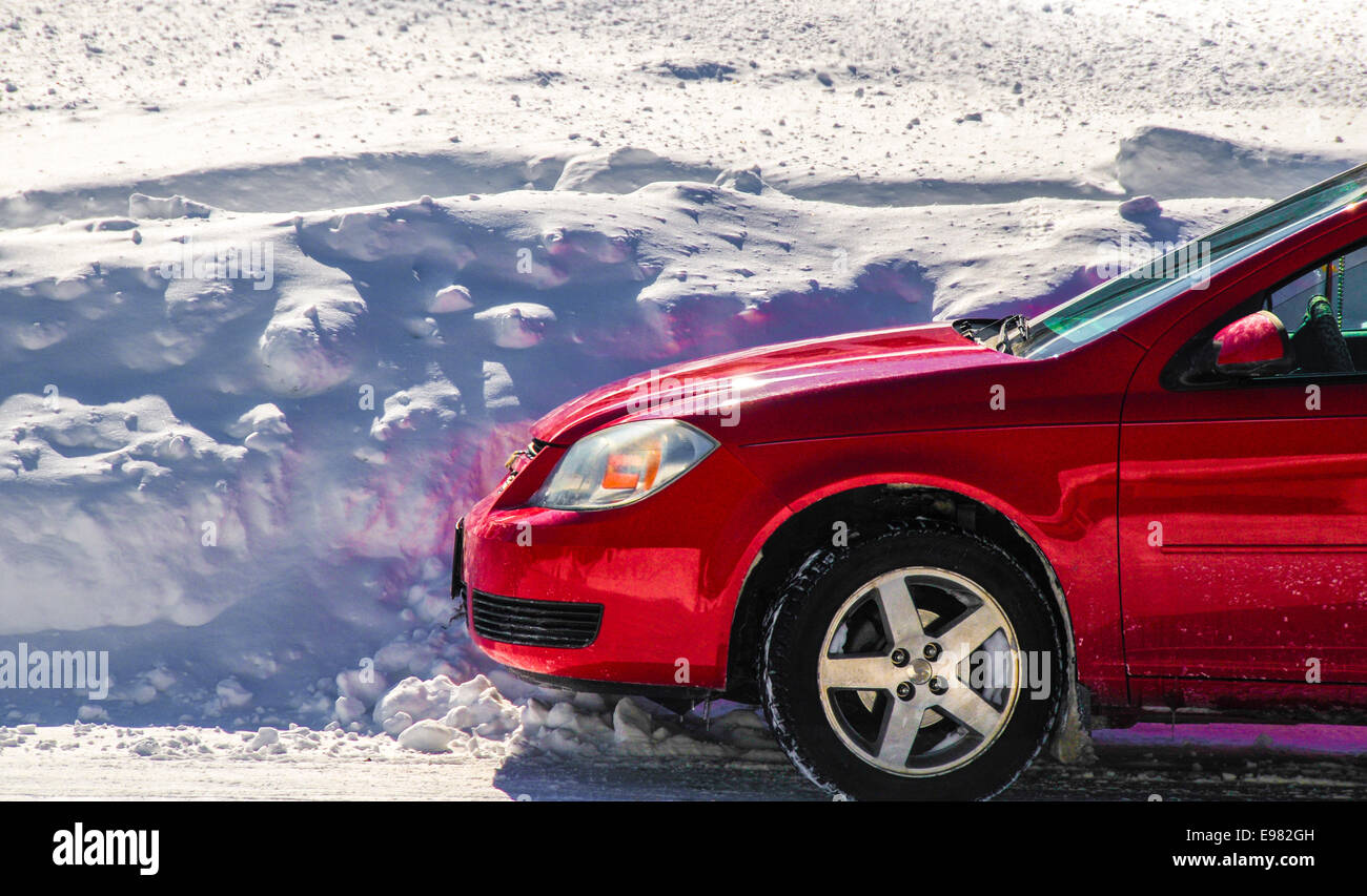 La parte anteriore di colore rosso brillante lucido pulito auto è parcheggiata di fronte 5 piedi di cumuli di neve bianca come la neve ombre blu. La neve riempie completamente immagine Foto Stock