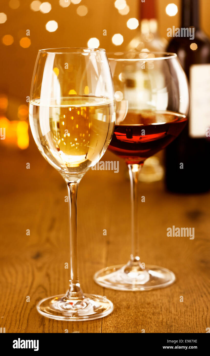 Celebrando con bicchieri di vino rosso e bianco contro una frizzante bokeh di festosa luci di partito Foto Stock