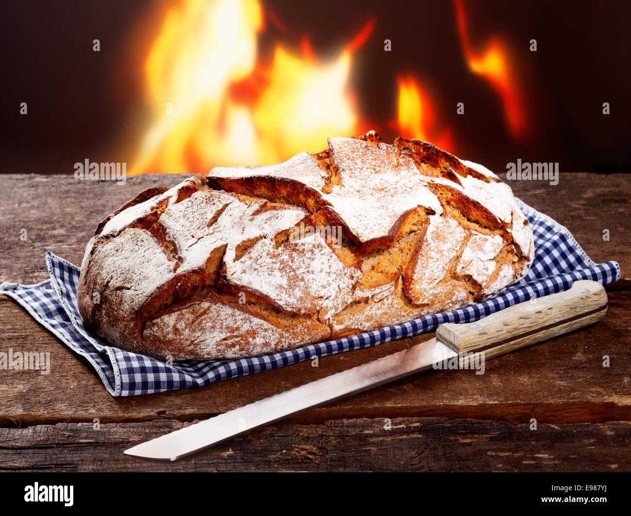 Croccante pagnotta di pane appena sfornato pane di segale con un coltello su un tovagliolo controllati davanti ad un fuoco fiammeggiante Foto Stock
