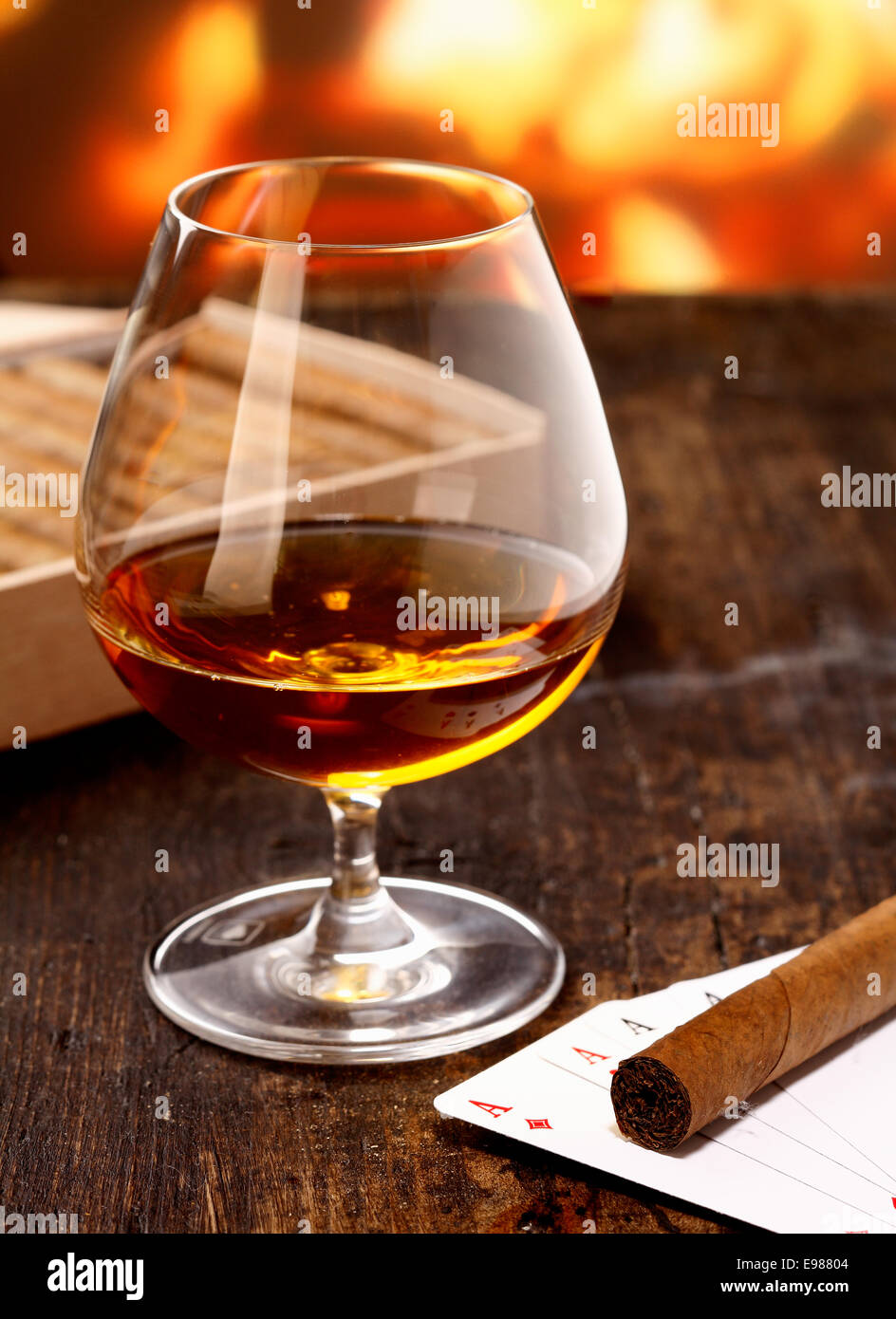 Il calice di cognac warming davanti al fuoco su un poker di notte con quattro assi e un sigaro Foto Stock