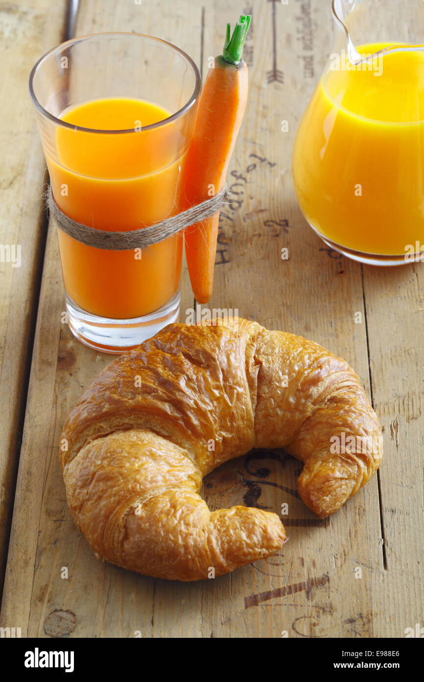 Millefoglie croccante golden croissant giacente su un vecchio trama da tavolo in legno con un bicchiere di succo di carota per uno snack sani Foto Stock