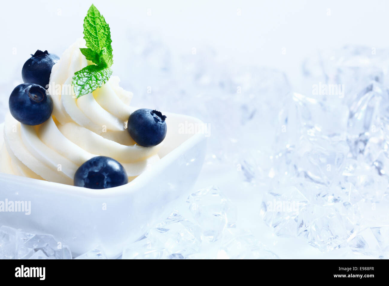 Mirtillo frozen yogurt con copia spazio. Con cubetti di ghiaccio e ghiaccio frantumato su fondo azzurro Foto Stock