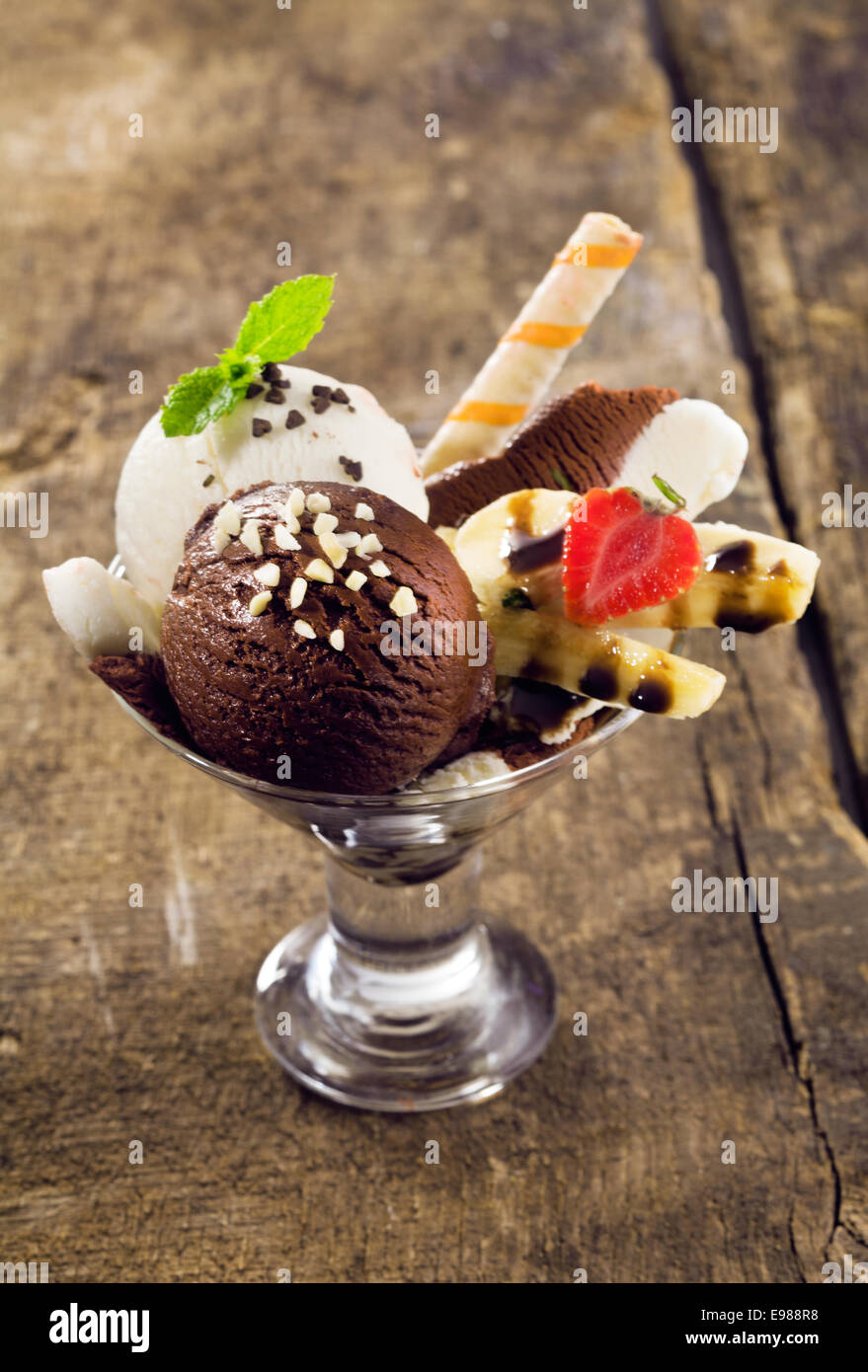 Palline di crema ricca di cioccolato e di gelato alla vaniglia e rabboccato con dadi su un maturo banana split in un bicchiere conico Foto Stock