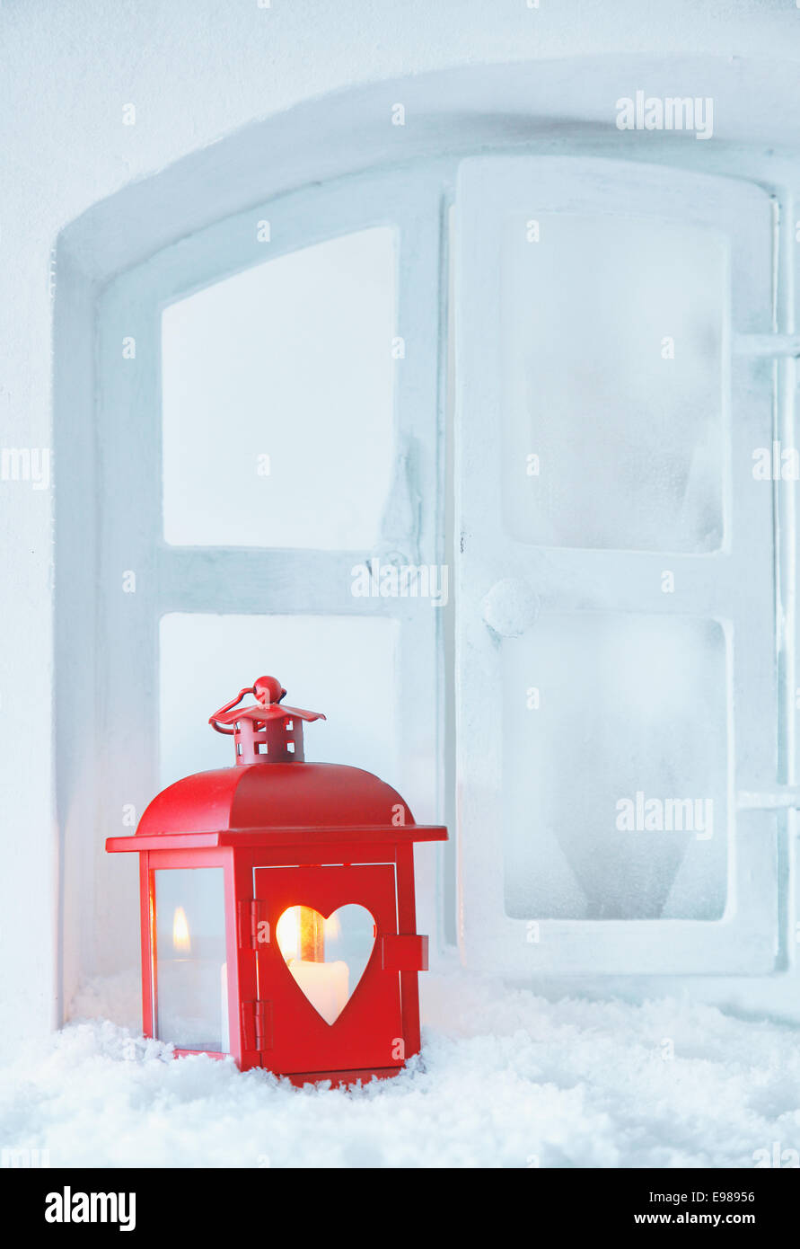 Allegro rosso lanterna di Natale con una candela incandescente in piedi su un davanzale innevato con copyspace stagionale per i messaggi di saluto Foto Stock