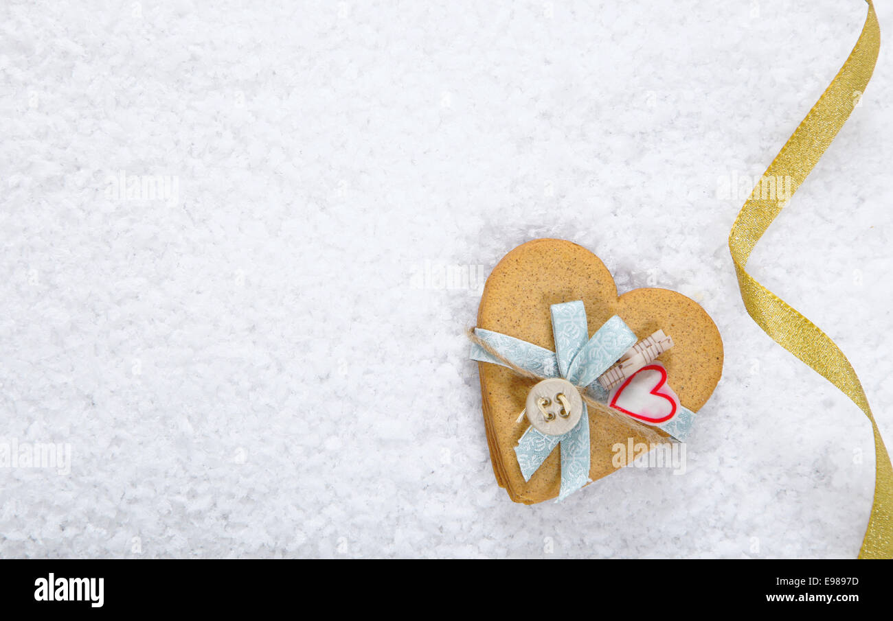 Sfondo di neve con un decorato a forma di cuore ad cookie e festoso nastro con copyspace per il tuo San Valentino o il messaggio di saluto di Natale Foto Stock