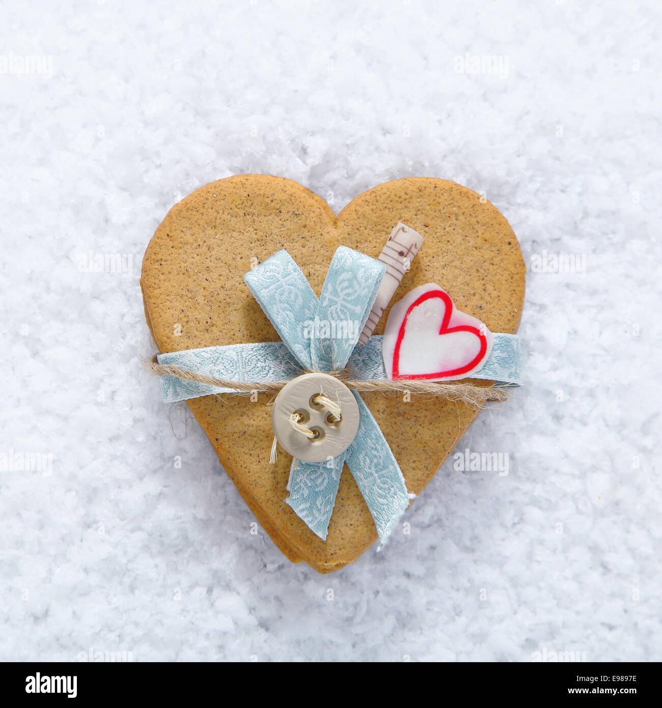 Biscotto decorativo cuore con fiocco e il pulsante su un letto di neve per il tuo San Valentino o natale vacanze auguri Foto Stock
