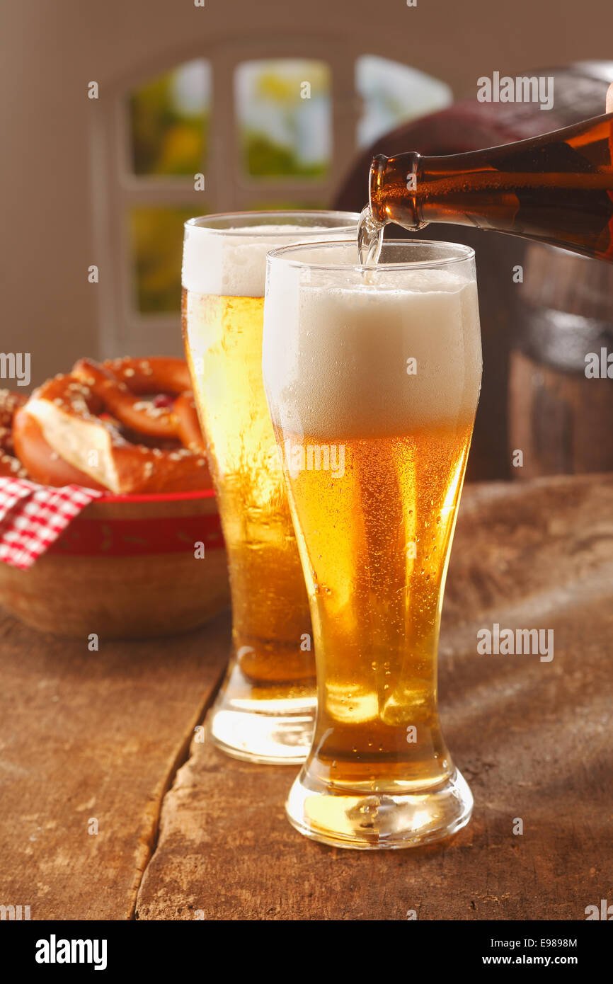 Versando bicchieri di Spumeggiante birra dorata in bicchieri alti da una bottiglia di vetro marrone in un pub o ristorante Foto Stock