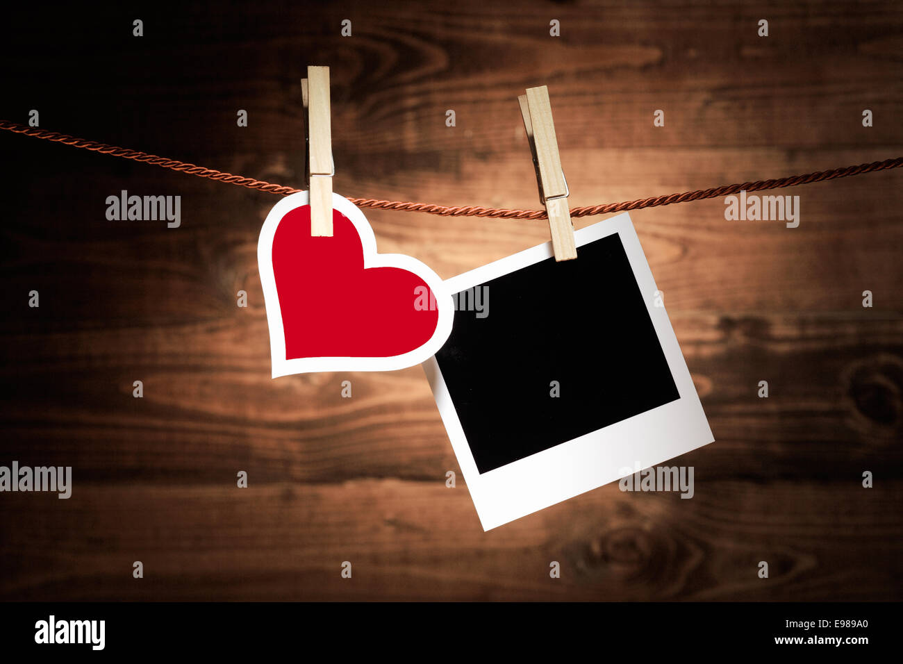 Un rosso e bianco cuore pende da una clothespeg in legno a fianco di uno sbozzato instant photo frame su un legno rustico sfondo per il vostro romantico nostalgici ricordi o messaggio di San Valentino Foto Stock