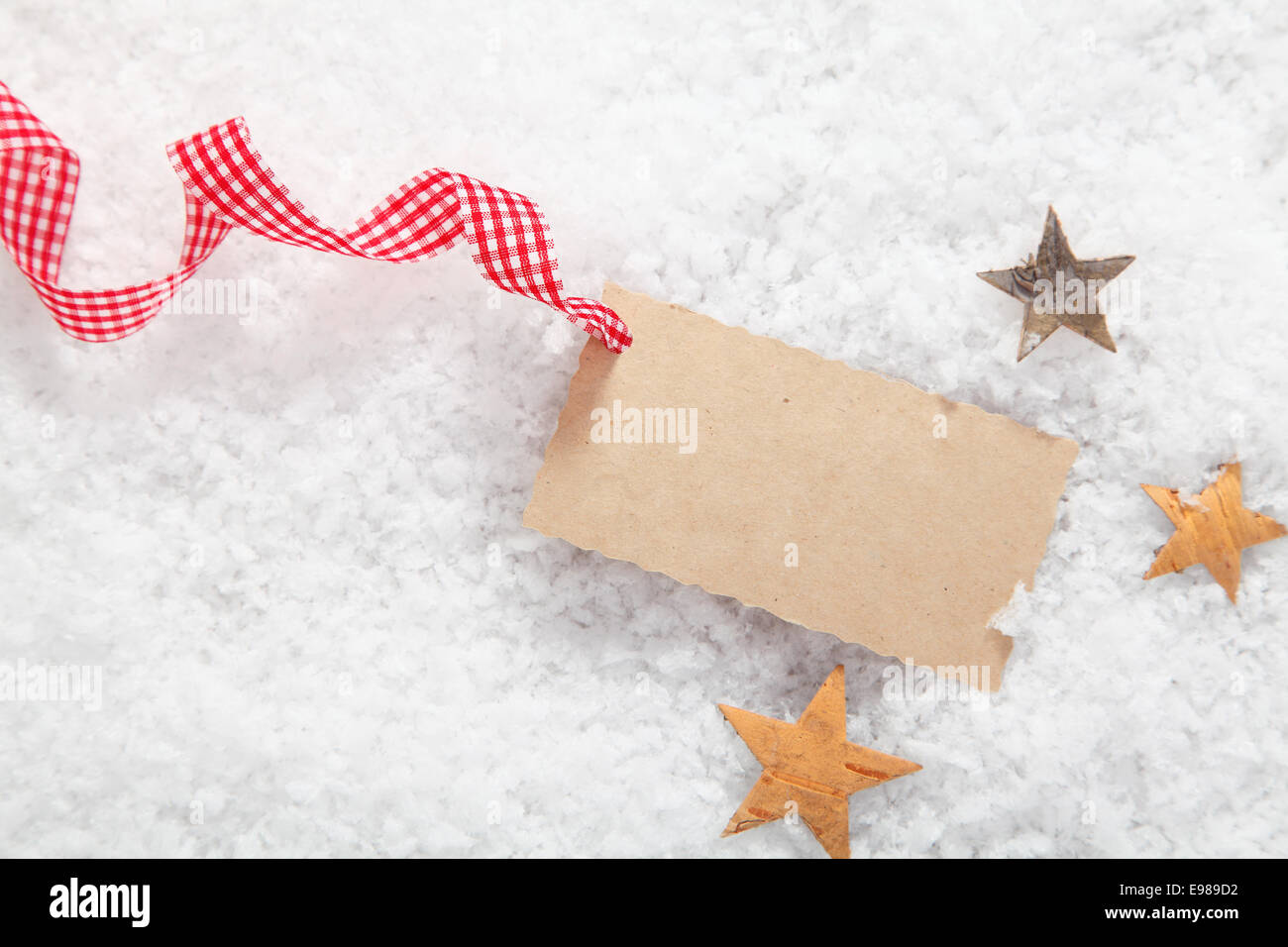 Vuoto dono di Natale etichetta decorativa con un rosso e bianco a scacchi nastro rustico circondato da stelle sulla neve fresca Foto Stock