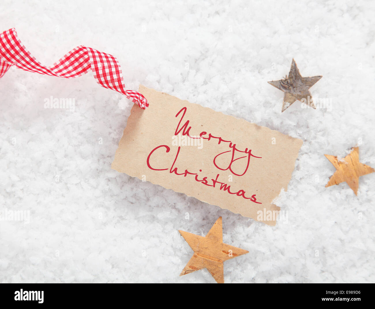 Tag regalo con buon Natale saluto e una decorazione rosso e bianco a scacchi nastro su un letto di neve invernale con le stelle Foto Stock